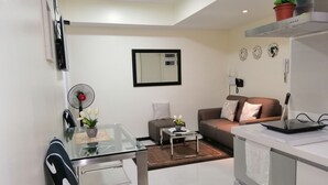 Un salon moderne comprenant une table à manger en verre, un canapé, une table basse et un coin cuisine avec un plan de travail et un évier.