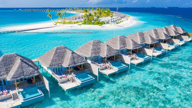 An overwater bungalows with thatched roofs, clear turquoise water, and a distant island with palm trees. - Sun Siyam Iru Veli - 24 Hours All-Inclusive (Aloofushi)