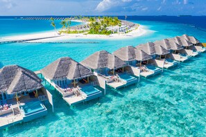 An overwater bungalows with thatched roofs, clear turquoise water, and a distant island with palm trees. - Sun Siyam Iru Veli - 24 Hours All-Inclusive (Aloofushi)