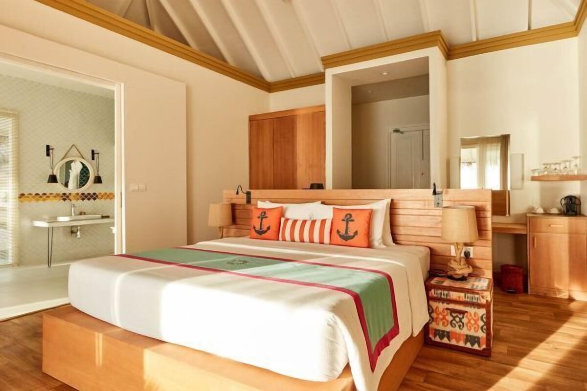 A bedroom with a bed, wooden headboard, bedside tables, a mirror, and a view of the bathroom.