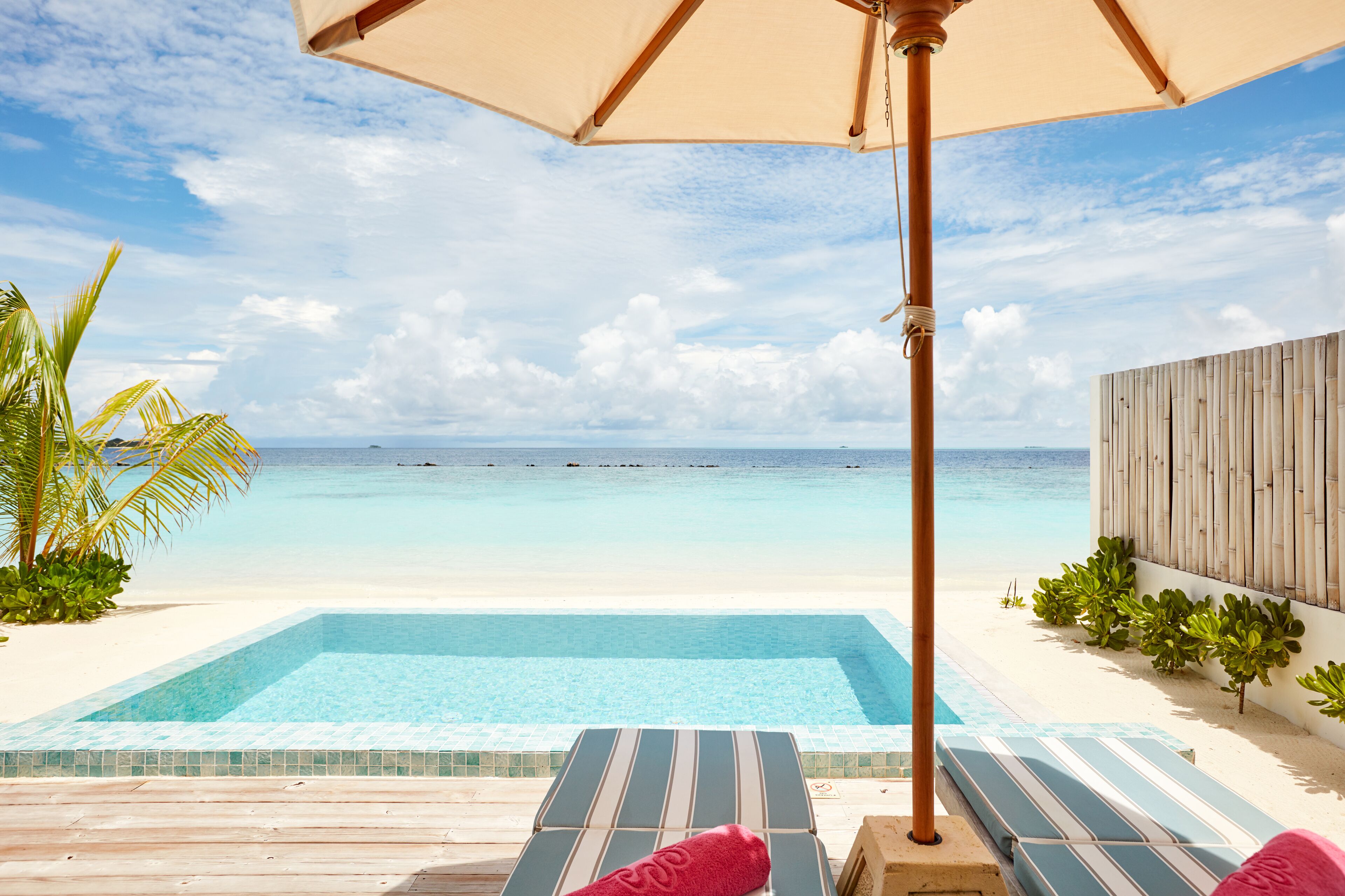 A poolside area with a view of the ocean, a wooden deck, and lounge chairs.