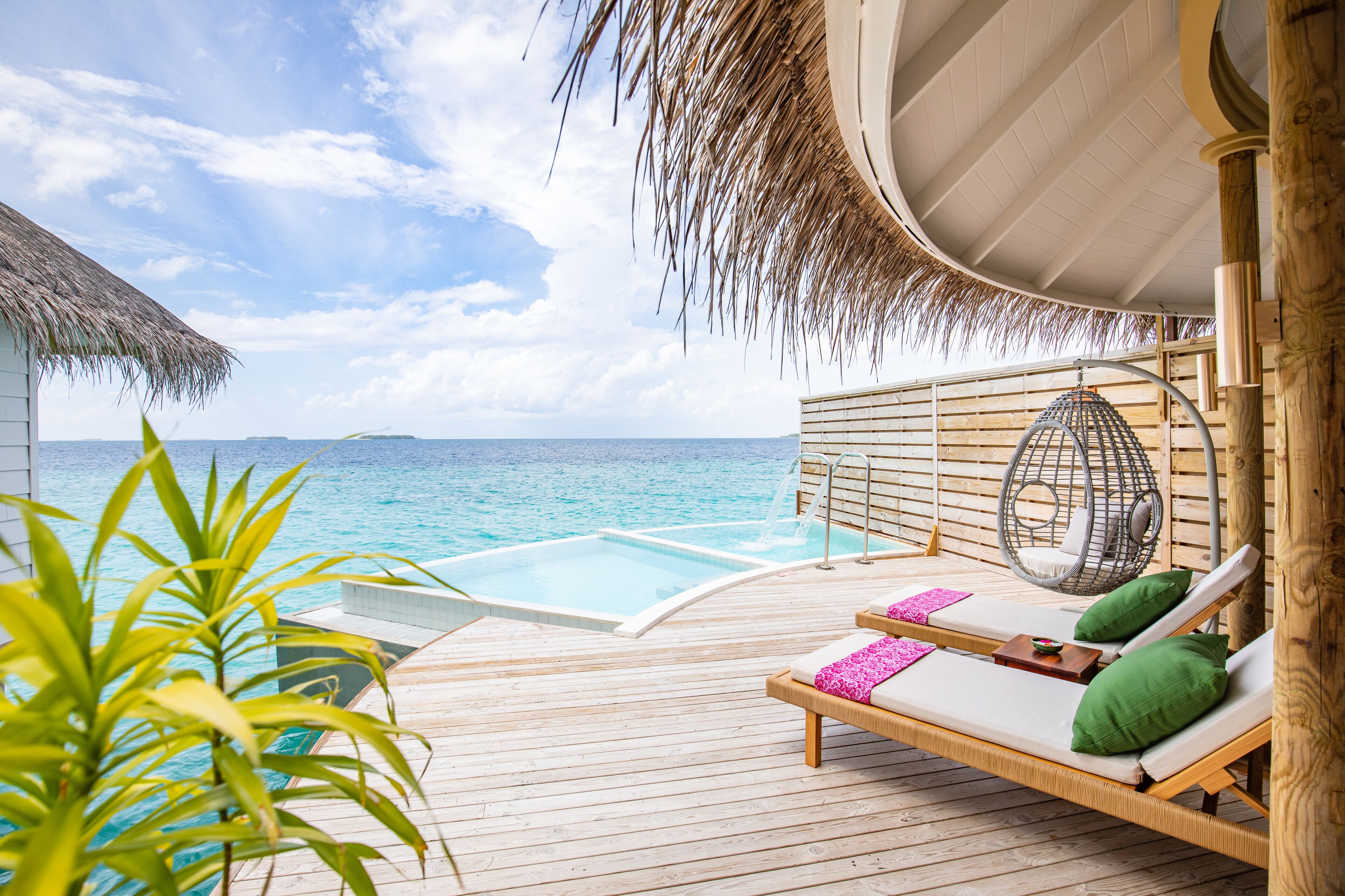 Une terrasse en bois avec une piscine, des chaises longues et un fauteuil suspendu offrant une vue sur l’océan.