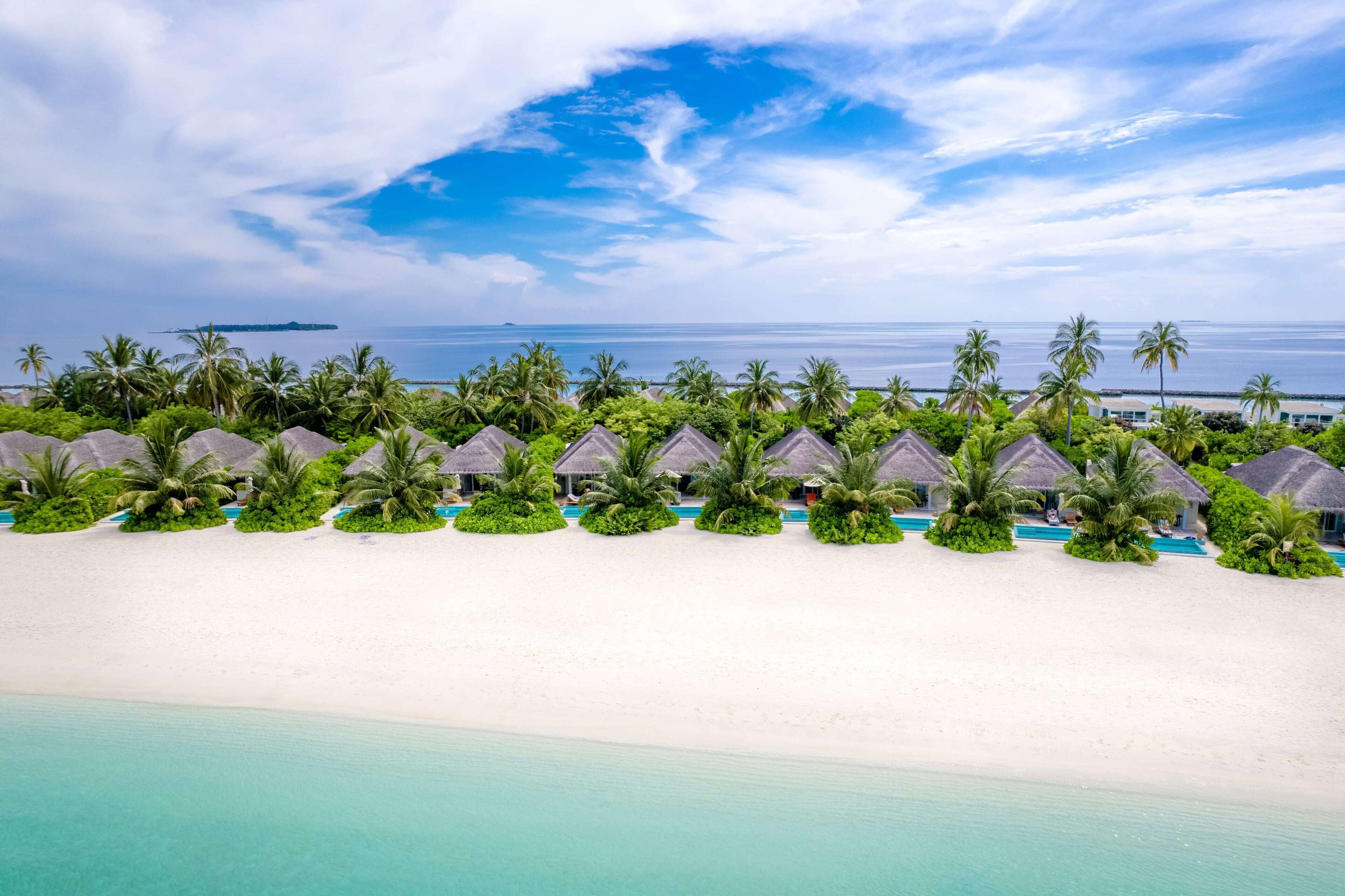 A beach resort with overwater bungalows, a white sandy beach, and a clear view of the ocean.