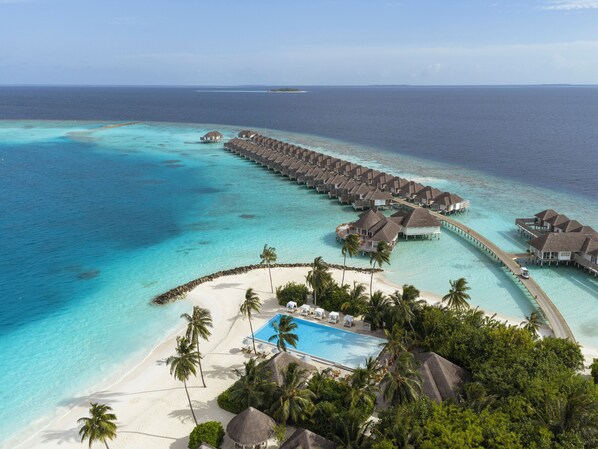 An overwater resort with multiple bungalow-style accommodations, a central swimming pool, and a beach area.