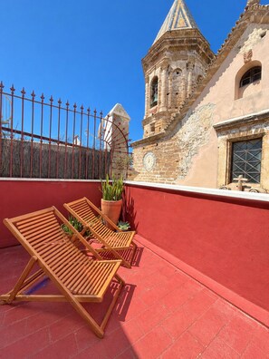 Une terrasse sur le toit avec deux fauteuils en bois, une plante en pot et un mur rouge.
