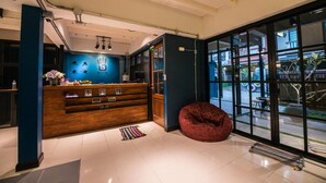 Un área de recepción con mostrador de madera, un sillón de ante rojo y grandes ventanales con vistas al exterior.