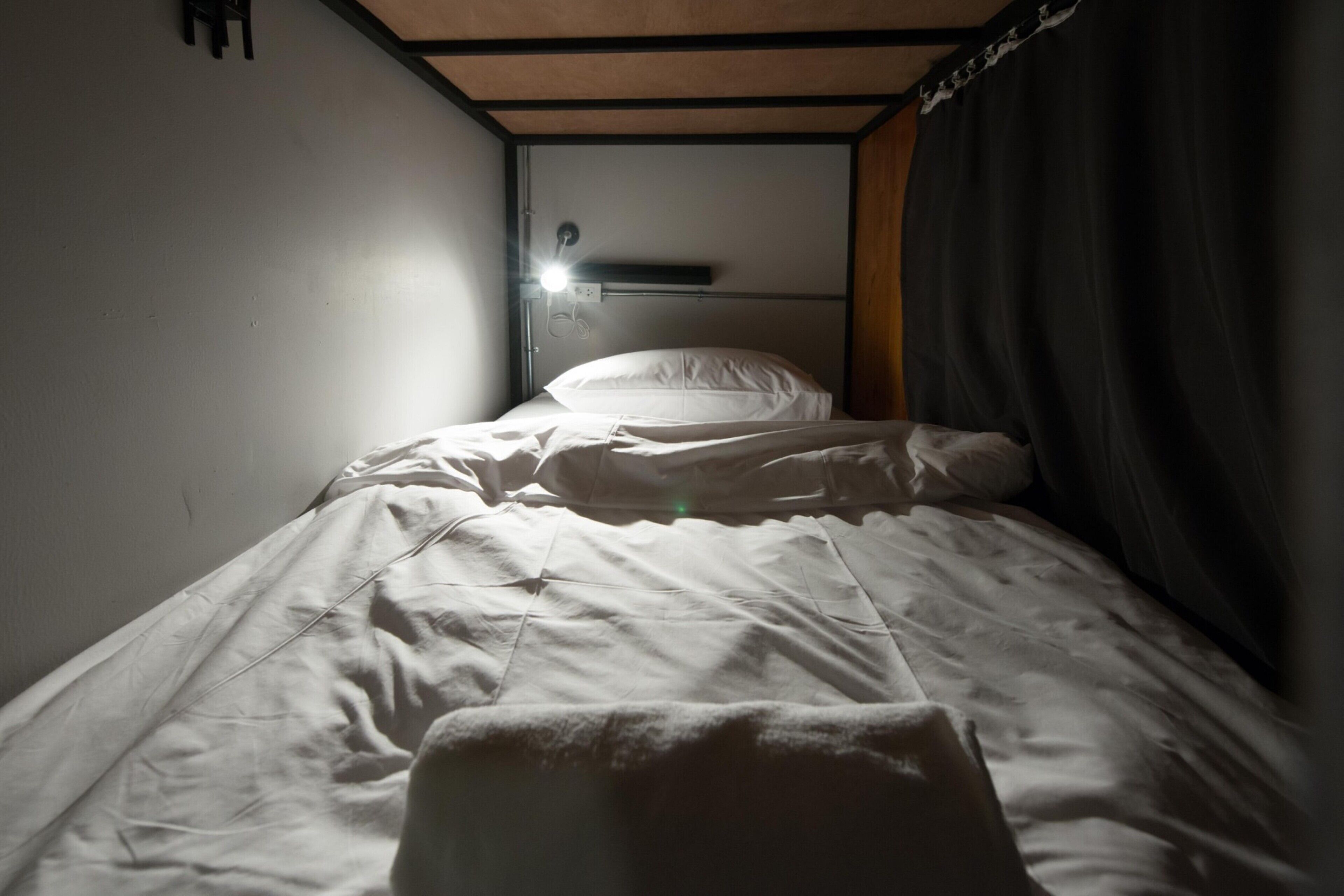 Una cama individual con ropa de cama blanca en una habitación con techo de madera y cabecera negra.