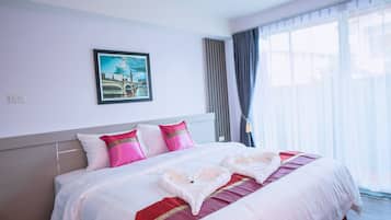 Habitación de hotel con una cama bien hecha, un cuadro enmarcado en la pared y un amplio ventanal con cortinas.