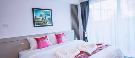 A hotel room with a neatly made bed, a framed picture on the wall, and a large window with curtains.