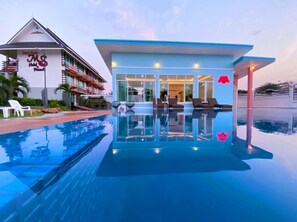 A hotel with a pool, lounge chairs, and a building with a blue roof.