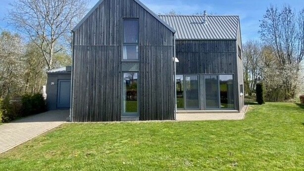 Un bâtiment moderne doté d’un toit en pente, de grandes fenêtres et d’une pelouse verdoyante.