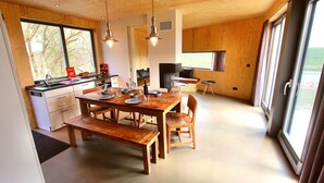 Une cuisine moderne avec des meubles en bois, une table à manger avec des bancs et de grandes fenêtres offrant une vue sur l’extérieur.