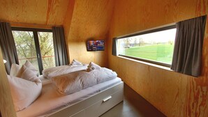 Une chambre à coucher avec un lit, un téléviseur fixé au mur et une fenêtre avec des rideaux.
