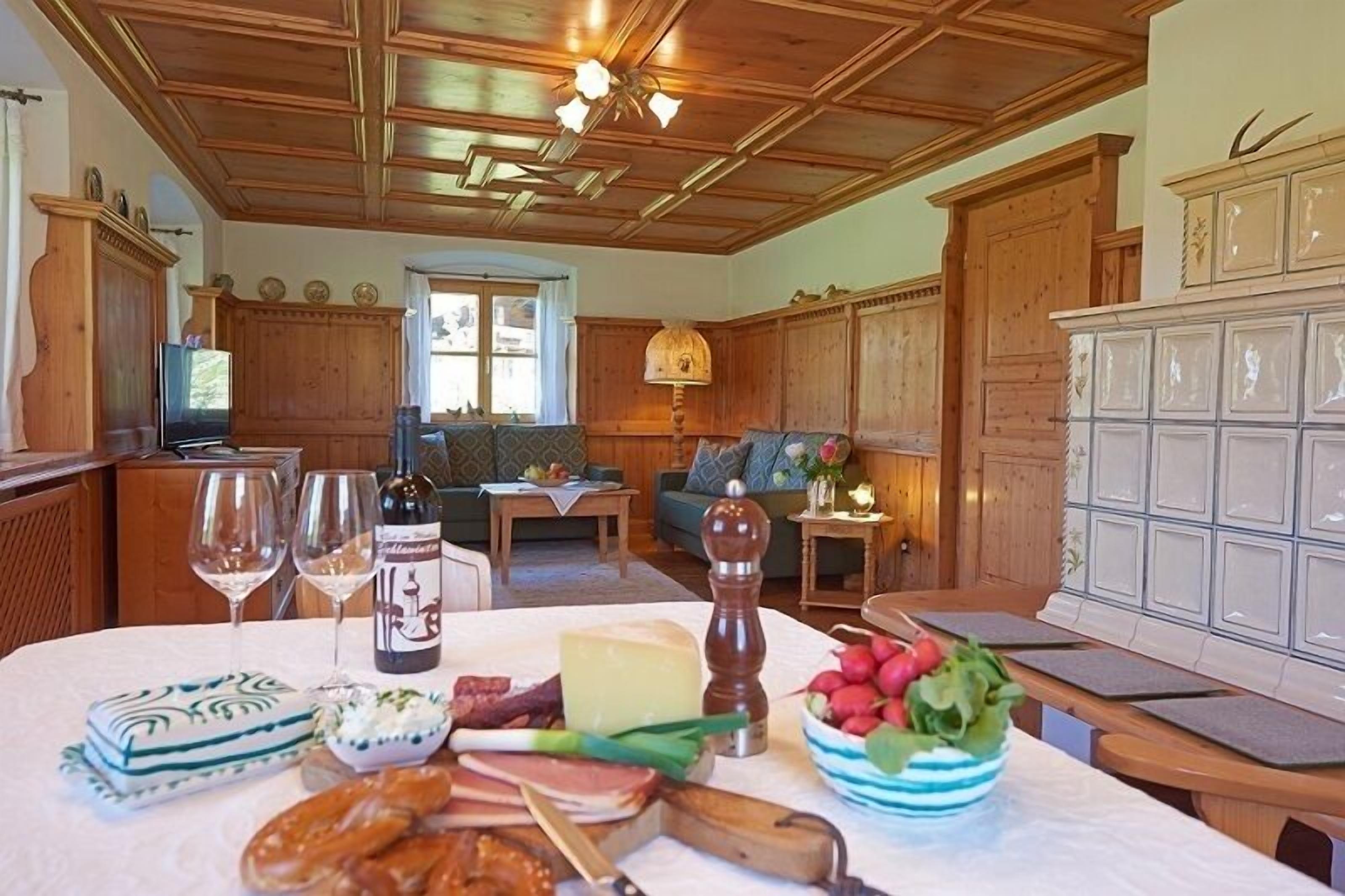 A dining area with a wooden table set for a meal, a sofa in the background, and a kitchen area with wooden cabinets.
