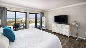 A bedroom with a large bed, a TV, a dresser, and a fan. - Surf Dweller 112🌊Gulf Front🏖️Free Beach Setup (Fort Walton Beach)