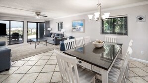 A spacious living area with a dining table, white chairs, and a sofa. - Surf Dweller 112🌊Gulf Front🏖️Free Beach Setup (Fort Walton Beach)