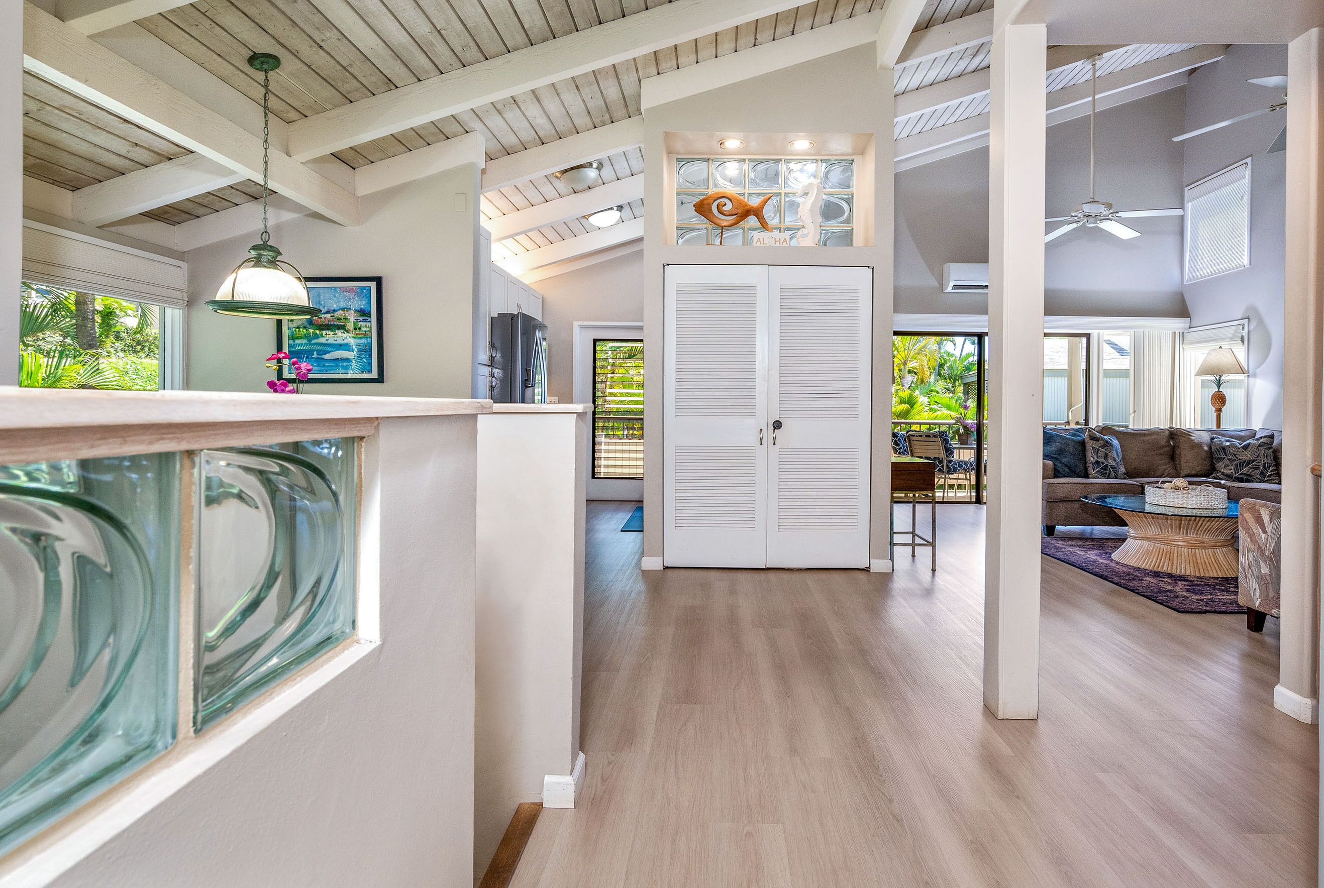 A spacious living area with a high ceiling, wooden beams, a dining area, and a view of greenery outside.