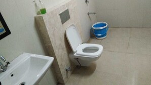 A bathroom with a toilet, sink, and a blue bucket. - Winsome Guest House (Noida)