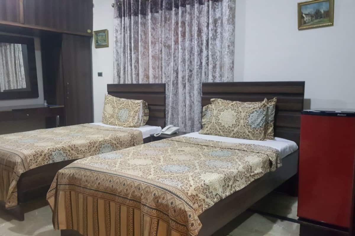 A room with two beds, each with patterned bedding, a small desk, a telephone, and a red cabinet.