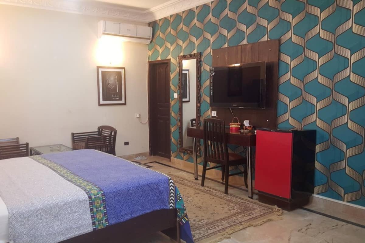 A bedroom with a bed, a desk, a chair, a TV, and patterned wallpaper.