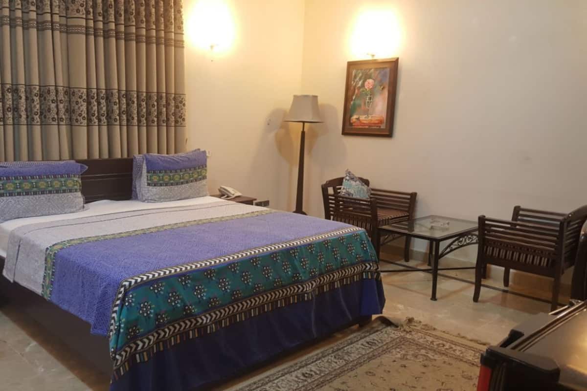 A bedroom with a bed, bedside table, lamp, chair, and a painting on the wall.