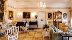 A formal living room with a piano, sofas, chairs, and a chandelier.