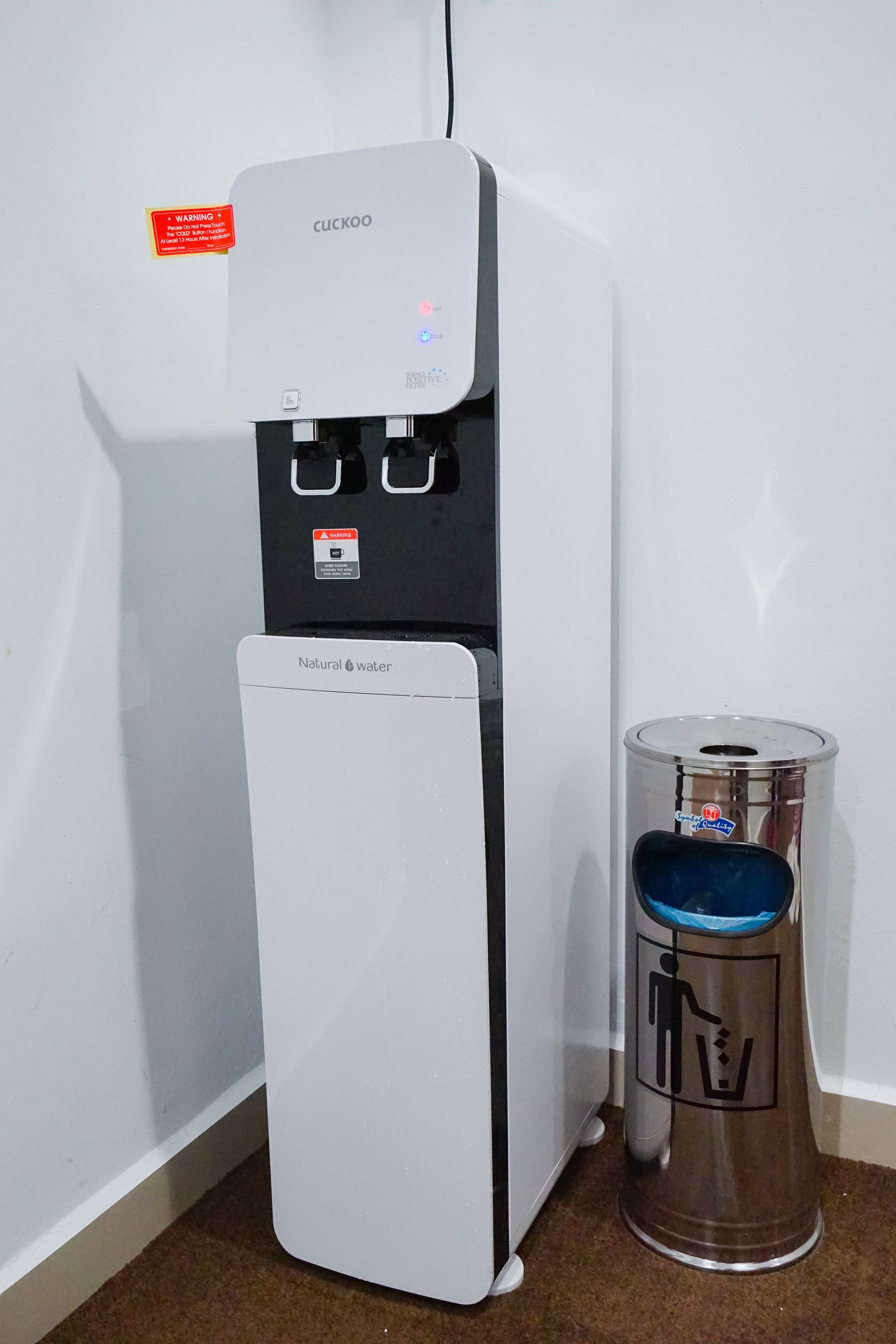 Un distributeur d’eau muni d’une étiquette d’avertissement et une poubelle portant le symbole du recyclage.