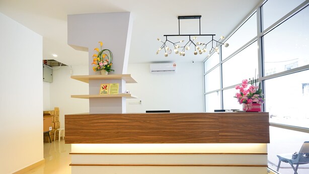 A modern reception desk with a wooden finish, a glass partition, and a large window offering a view of the outside. - Grand FC Hotel (George Town)