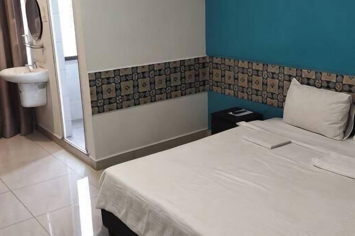 Ein Hotelzimmer mit einem Bett, einem Waschbecken, einem Spiegel, einem Fenster mit Vorhängen und einer gefliesten Wand.