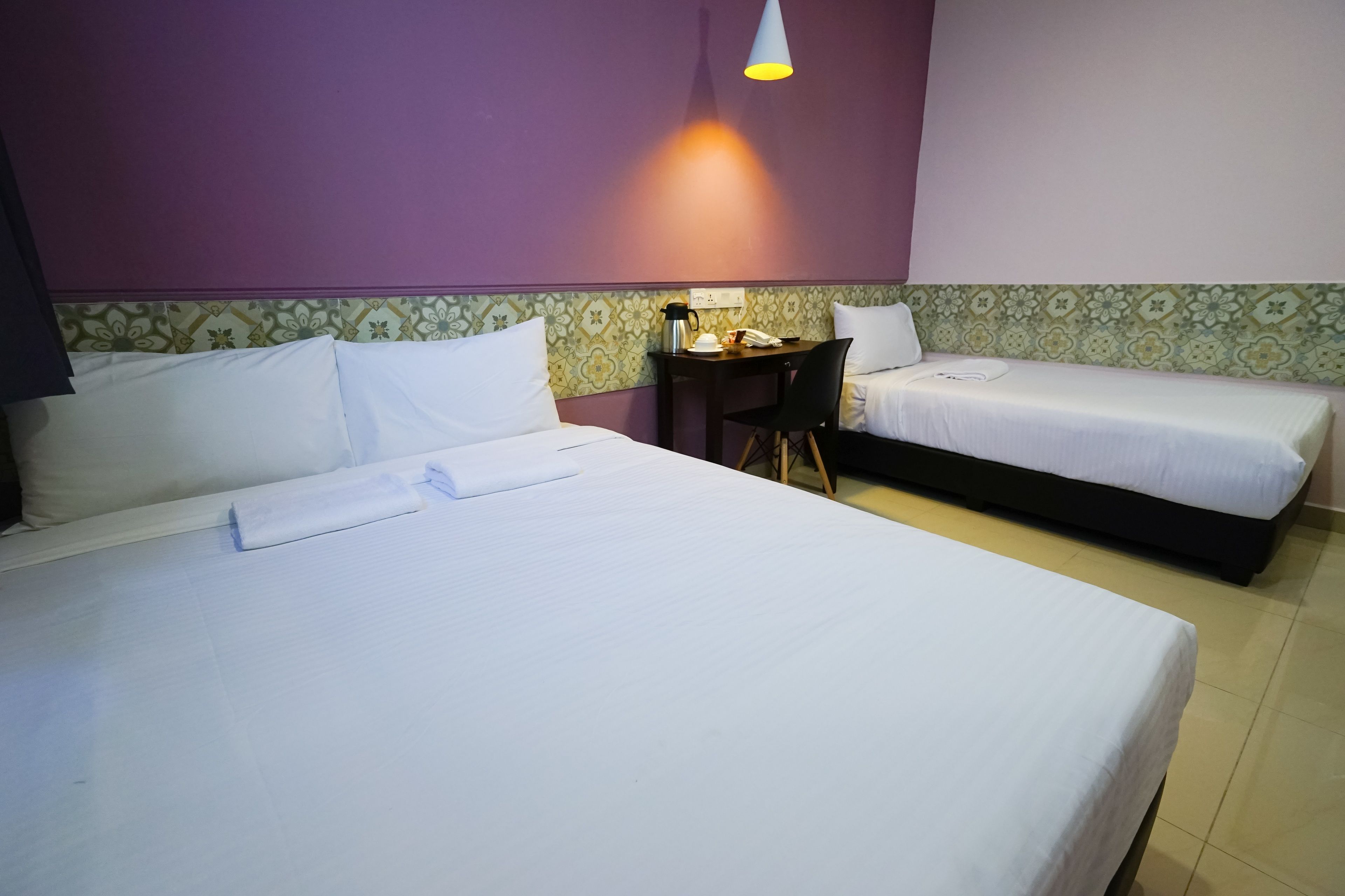 A hotel room with two single beds, a small desk with a chair, and a table with a kettle and a cup.