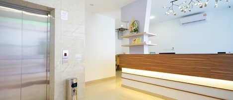 A modern reception area with a wooden reception desk, a marble wall, and an elevator.