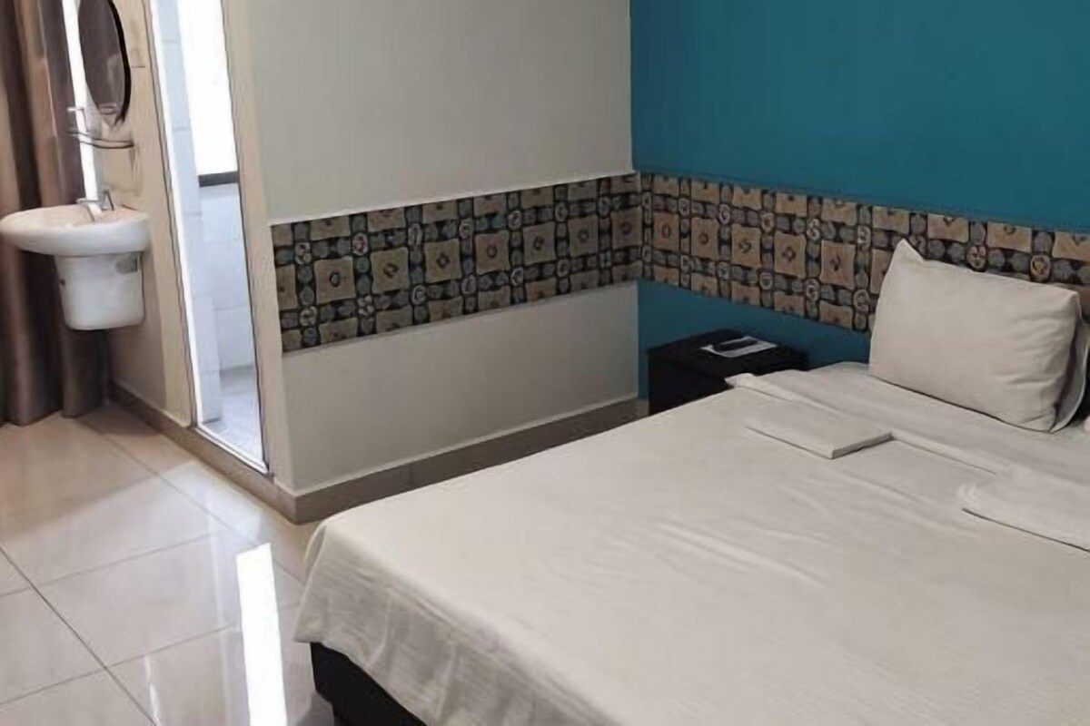 A hotel room with a bed, a sink, and a window with curtains.