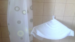 Casa de banho com cortina de chuveiro estampada com círculos e uma toalha branca pendurada num porta-toalhas fixado na parede.