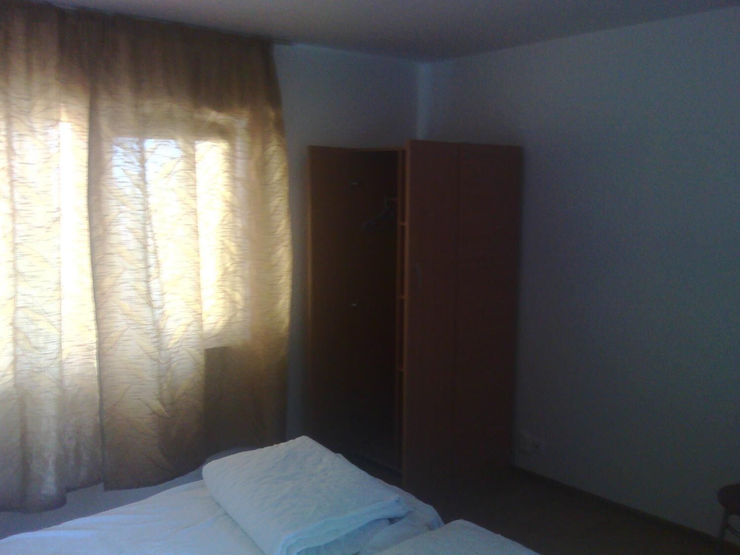 Een hotelkamer met een bed, een kledingkast en een raam met gordijnen.