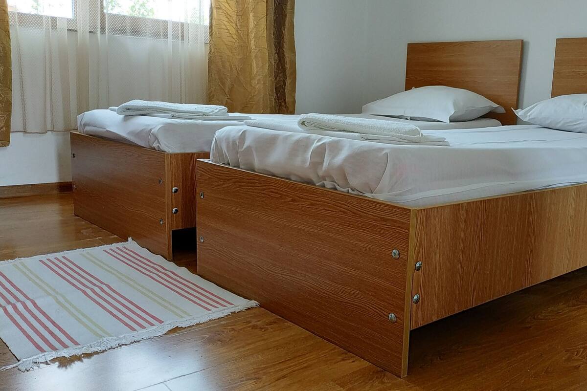 A double wooden bed with white linens and pillows, a wooden nightstand, and a striped rug on a wooden floor.