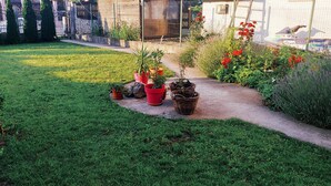 Um jardim bem cuidado, com diversos vasos de plantas e flores, um caminho bem definido e um cercado delimitando o espaço.