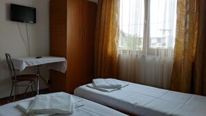 Quarto de hotel com duas camas, uma escrivaninha com cadeira, televisão na parede e janela com cortinas.