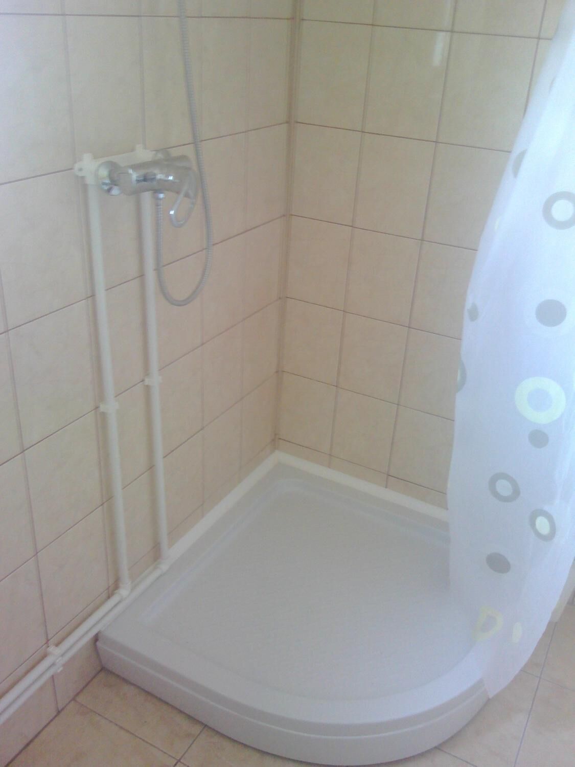 A small, enclosed shower area with tiled walls and floor, a showerhead, and a curtain with a polka dot pattern.