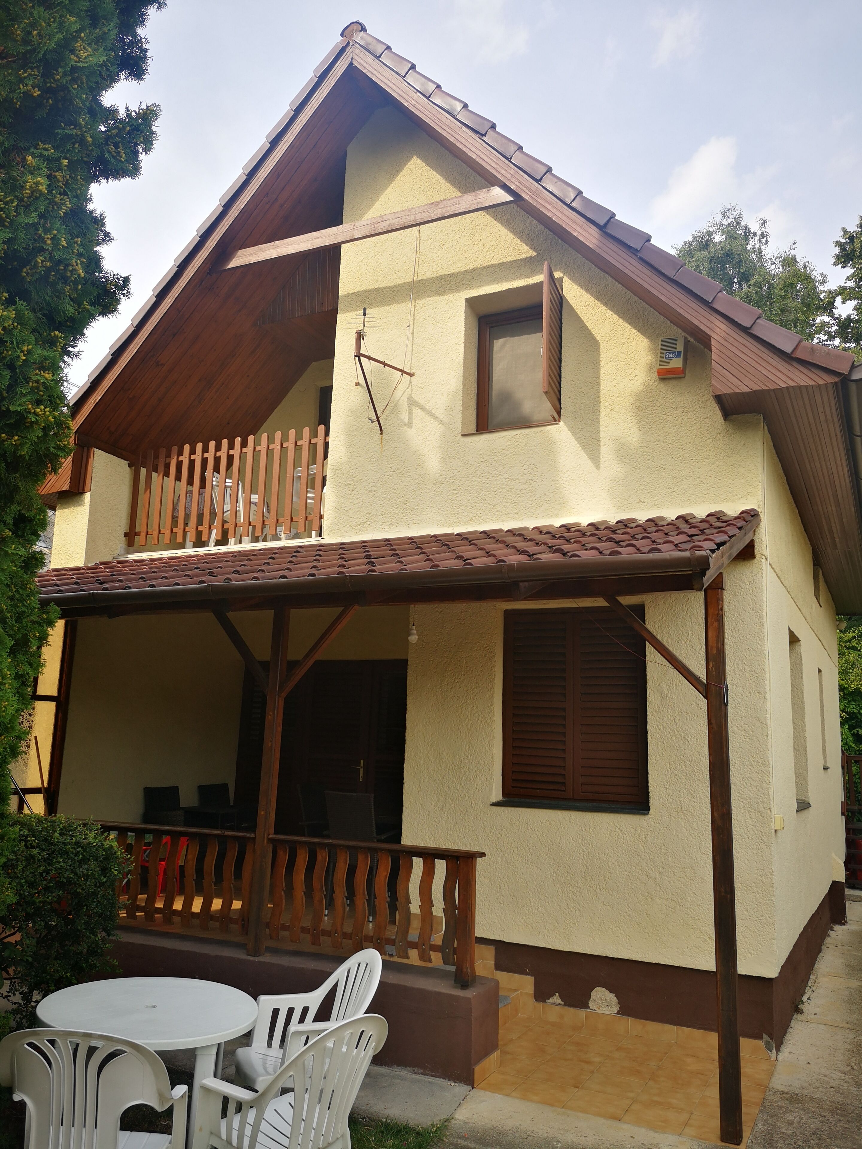 Ein zweistöckiges Haus mit Balkon, kleiner Veranda und Ziegeldach.