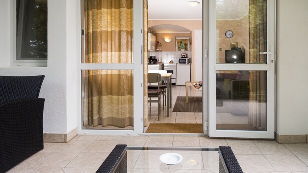 Una sala de estar con un sofá, una mesa de centro de vidrio y un ventanal corredero que da a una zona de cocina.