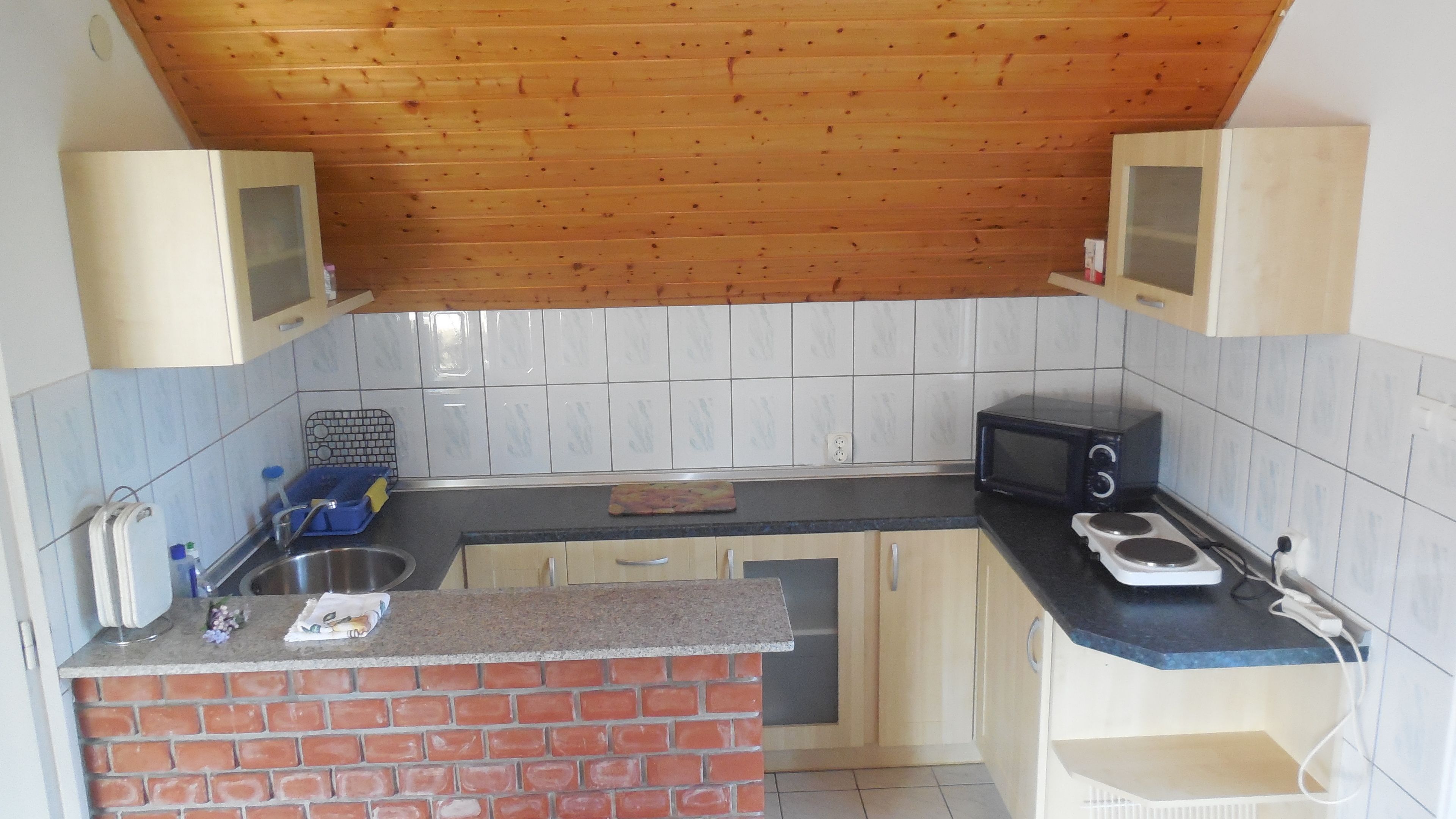 A compact kitchen with a brick backsplash, a microwave, and a sink.