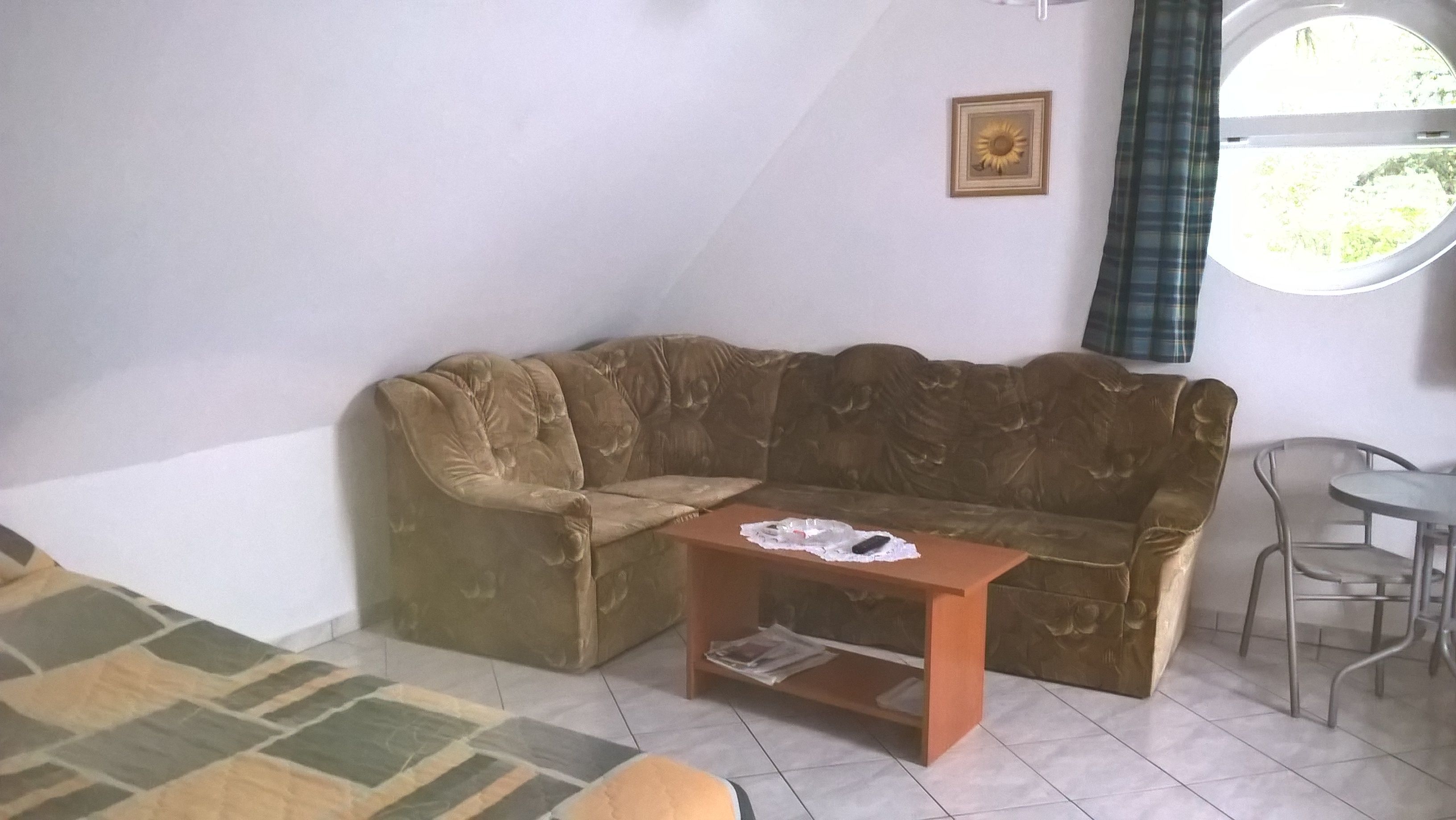 A living room with a brown sofa, a small wooden table, a metal chair, and a window with a curtain.