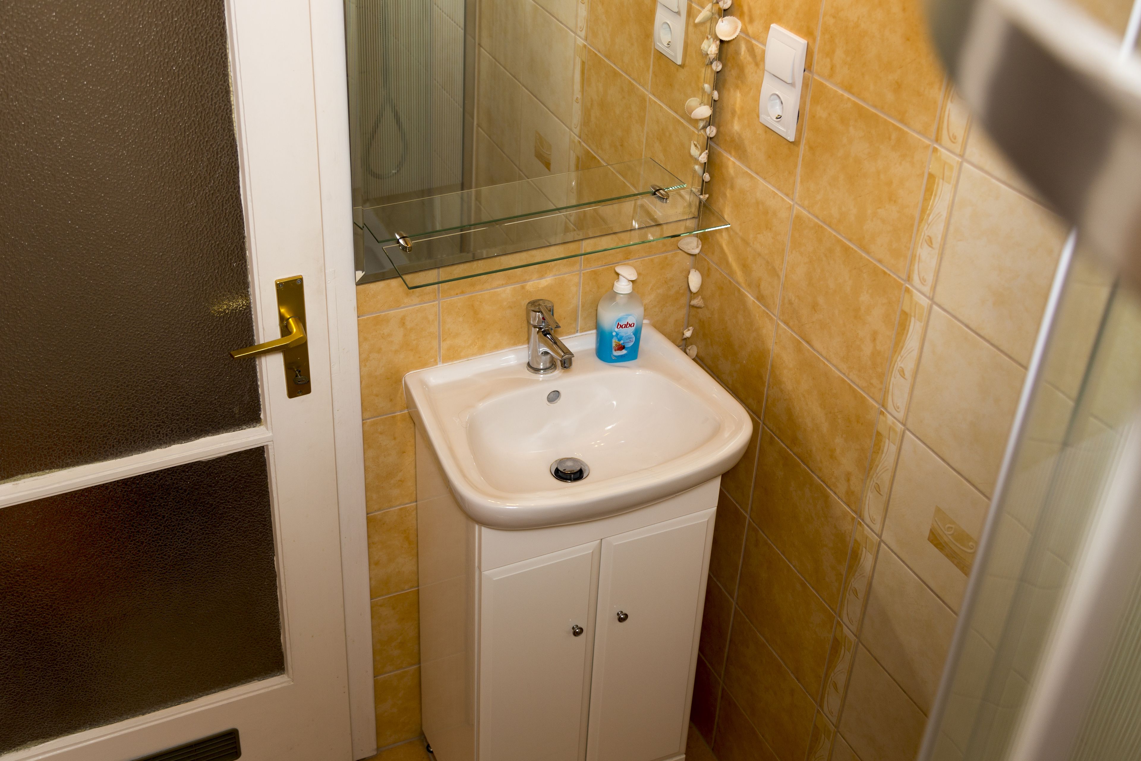 A bathroom with a white sink, a glass shelf above it, and a mirror.