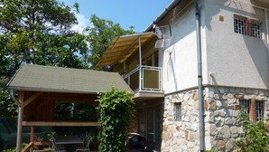 Una casa de dos pisos con fachada de piedra, una terraza de madera con mobiliario exterior y un balcón.