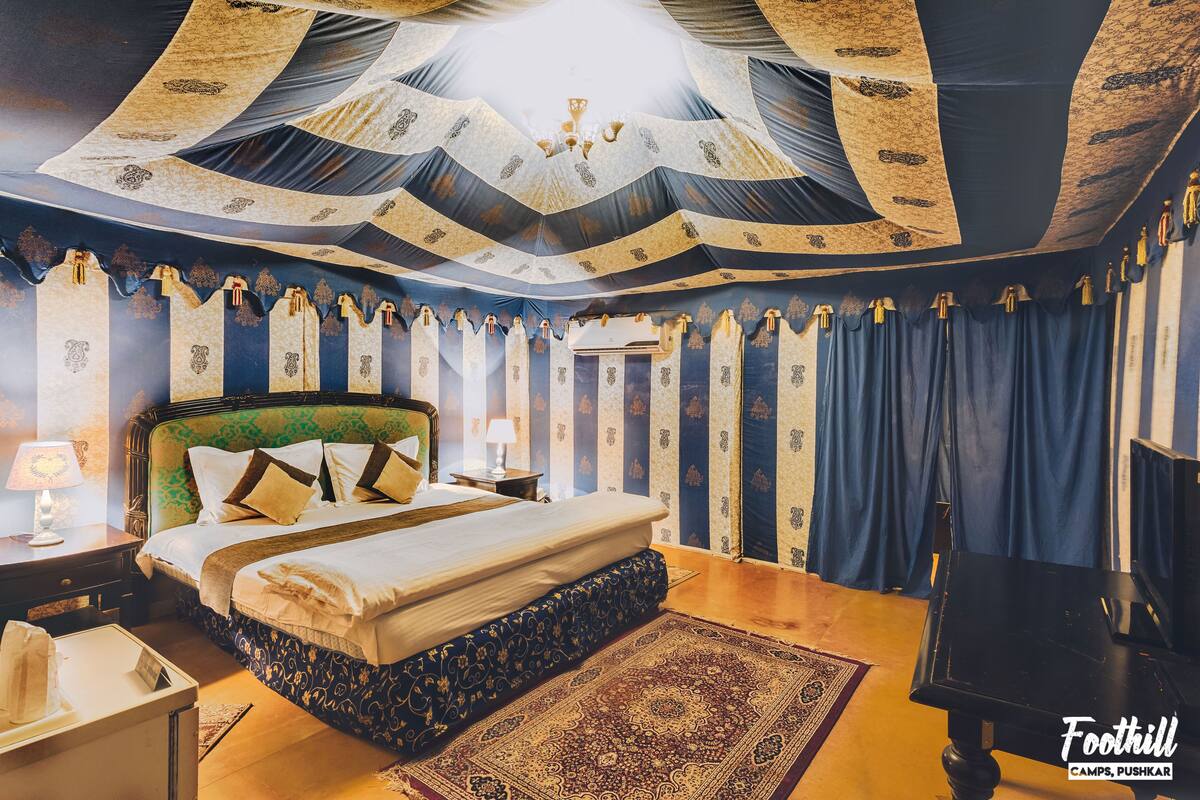 A bedroom with a large bed, a nightstand, a lamp, a TV, and a patterned rug.
