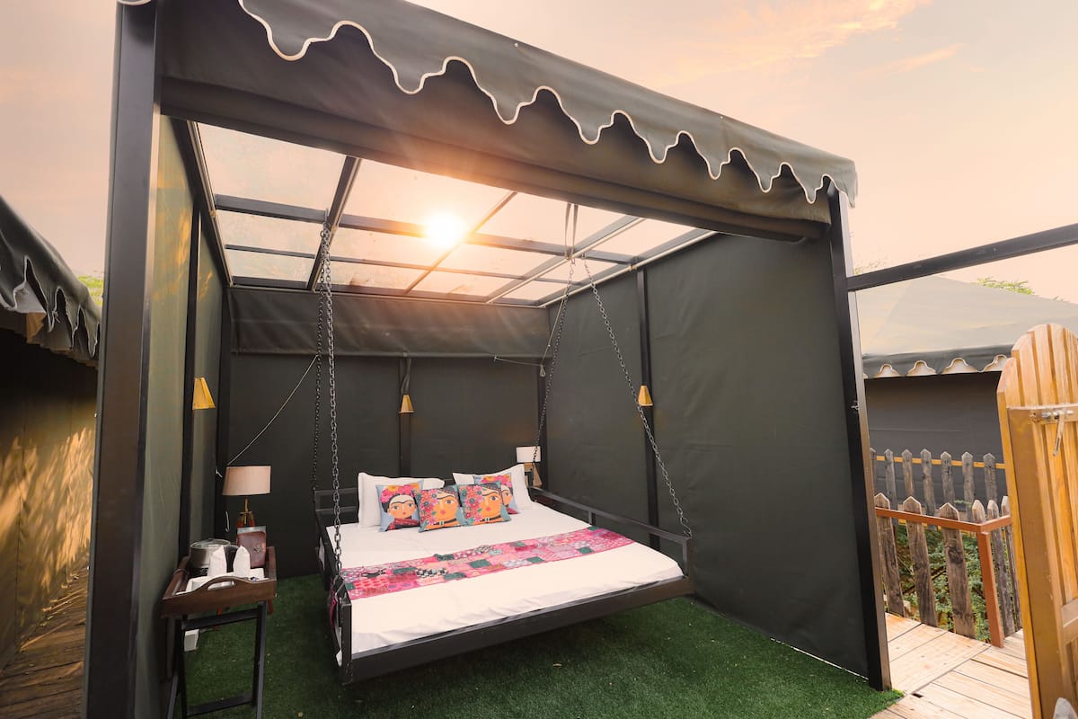 A bedroom with a bed, bedside table, lamp, and a view of the outdoors.