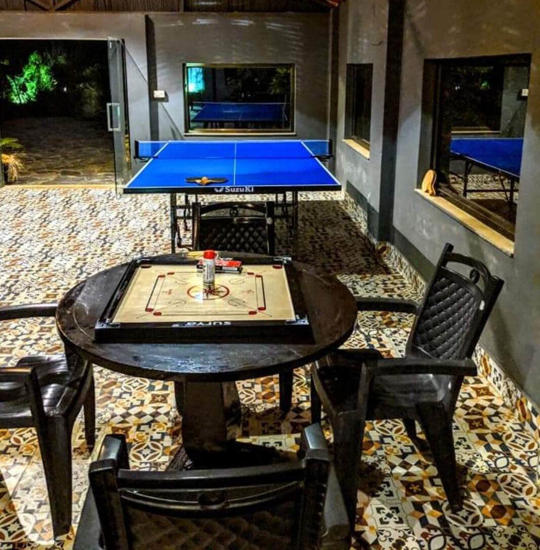 Una mesa de ping pong con superficie azul, rodeada de sillas y una mesa con un tablero de juego.