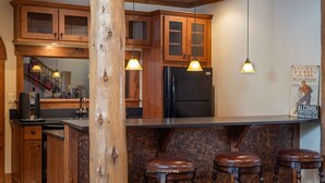 Cozinha com armários de madeira, geladeira preta, máquina de café e um balcão com banquetas.