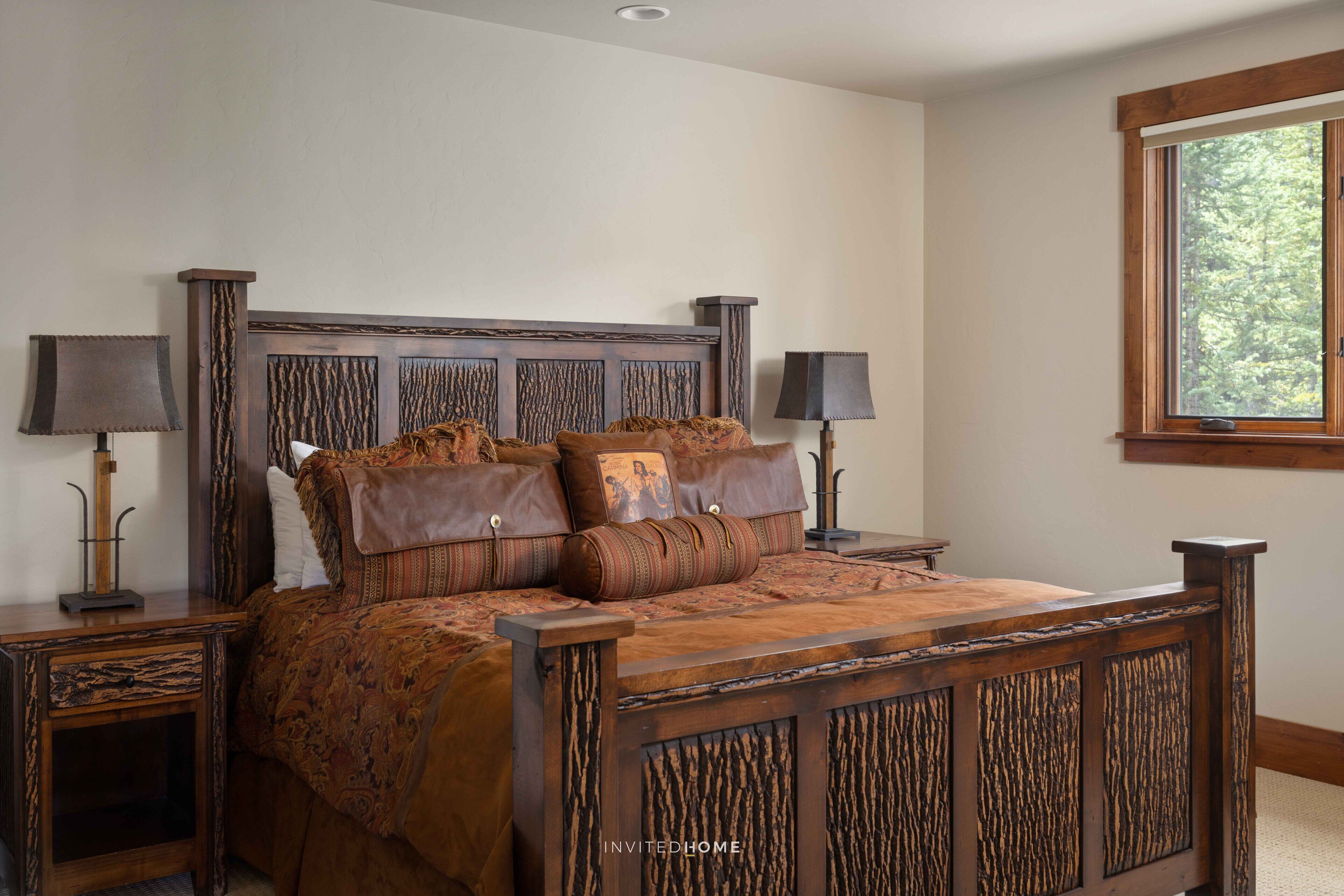 Un dormitorio con una cama de madera, dos mesitas de noche con lámparas y una ventana con vistas a árboles.