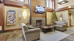 A spacious lobby with a fireplace, comfortable seating, a Christmas tree, and a television mounted on the wall.